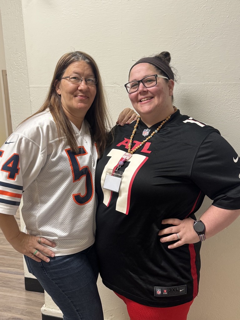 Two women stand next to each other; one wears a white football jersey, the other a black one.