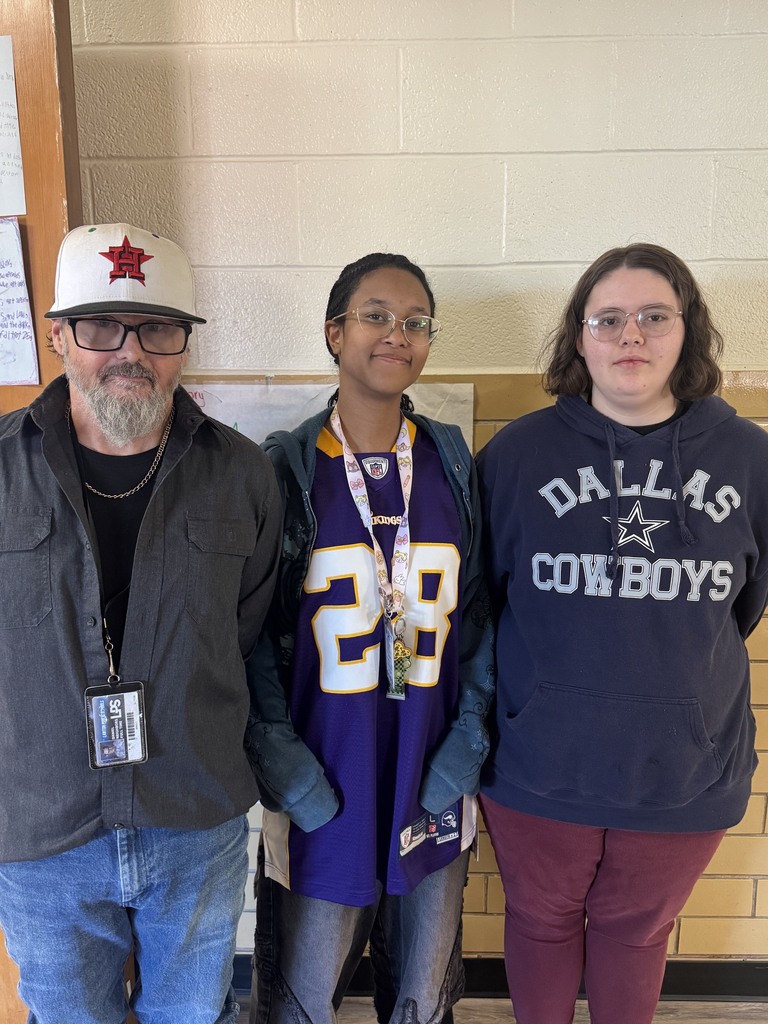 Three people standing in a hallway. A man wearing a baseball cap, a woman with glasses, and another woman in a blue sweatshirt.