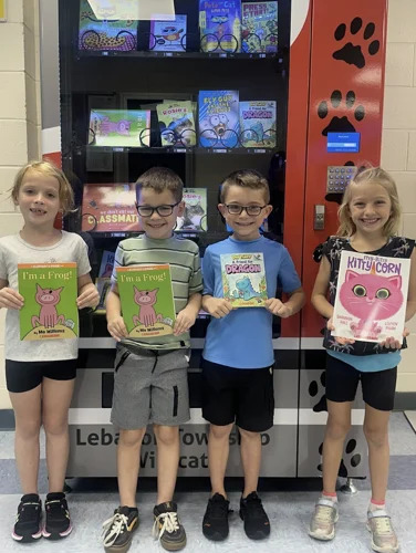 picture of four students holding books in front of a vending machine