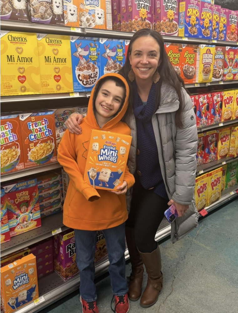 picture of a boy and his mom holding a ceral box he designed in the grocery store