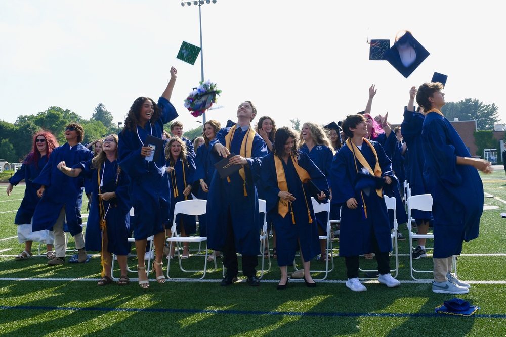 Happy graduates in navy blue gowns toss their caps in the air