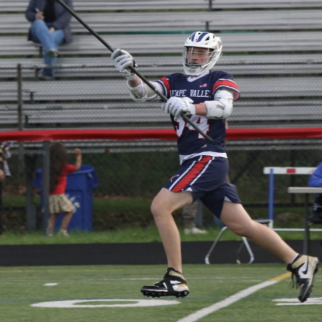 Jaxson Goss runs across the lacrosse field in a Lenape Valley navy, red, and white uniform and helmet, holding his lacrosse stick.