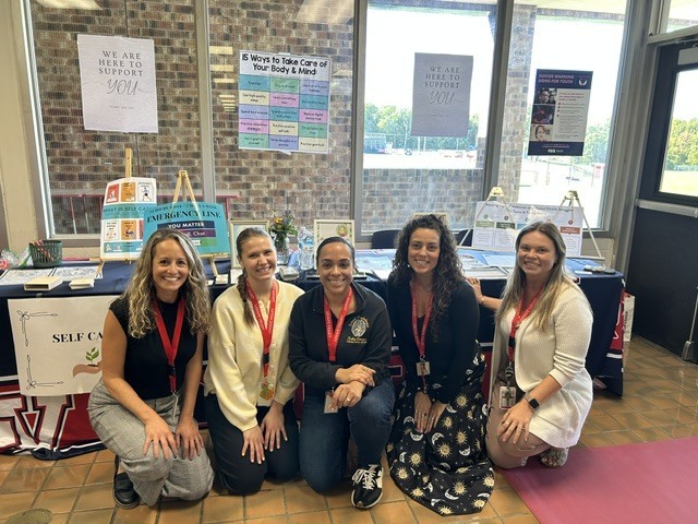 Five members of Lenape Valley’s school clinical team pose together in front of a resource table featuring mental health, wellness, and self-care materials for students.