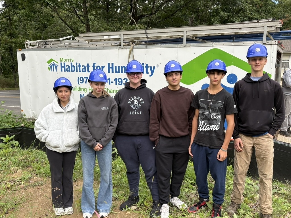 Six Lenape Valley students wearing blue hard hats pose in front of a Morris Habitat for Humanity truck while participating in a community service project.