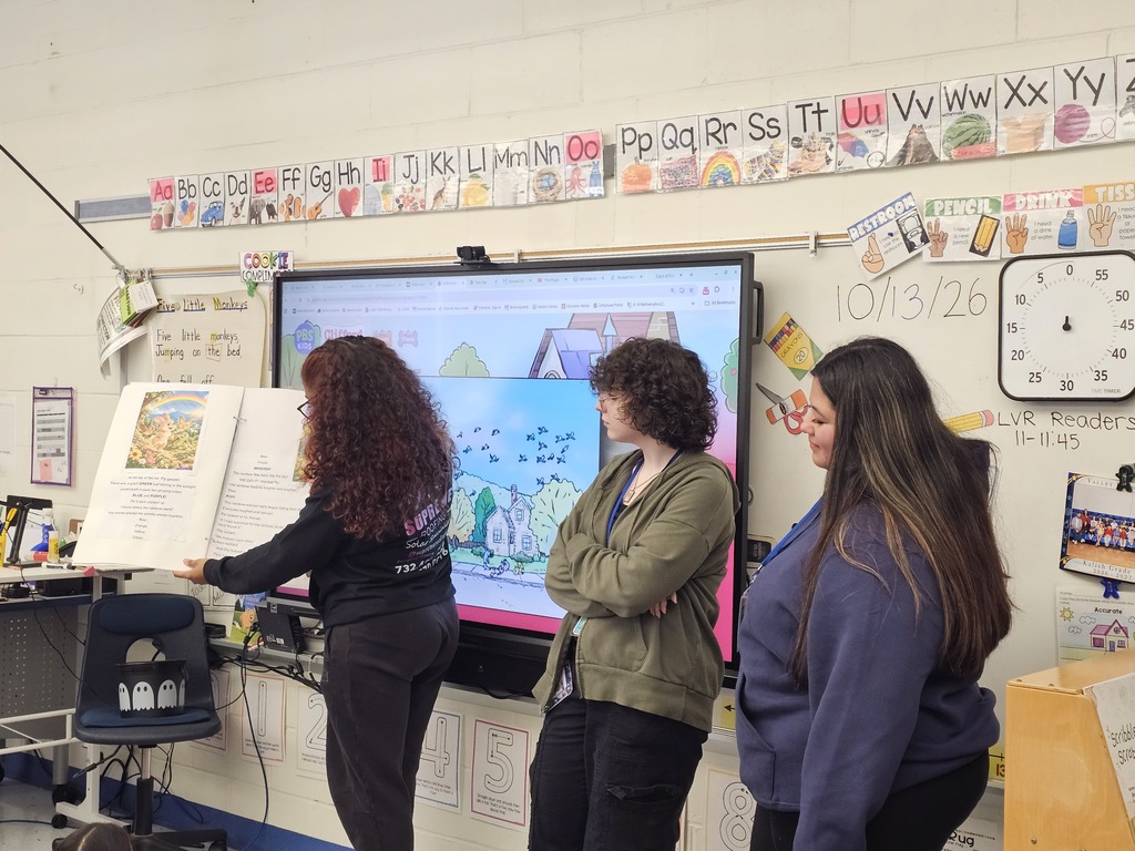 Three Lenape Valley Foundations of Education students present “Pip and the Missing Rainbow” in a Stanhope Elementary classroom, with one holding the illustrated book open for young listeners.