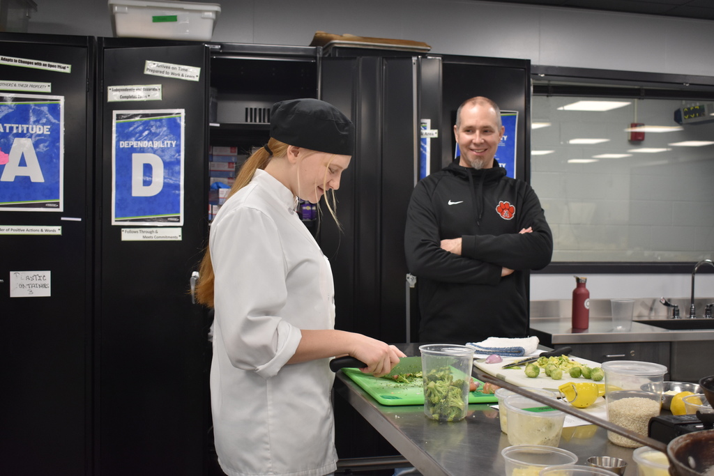 Culinary student chopping food for demonstration while visitor watches