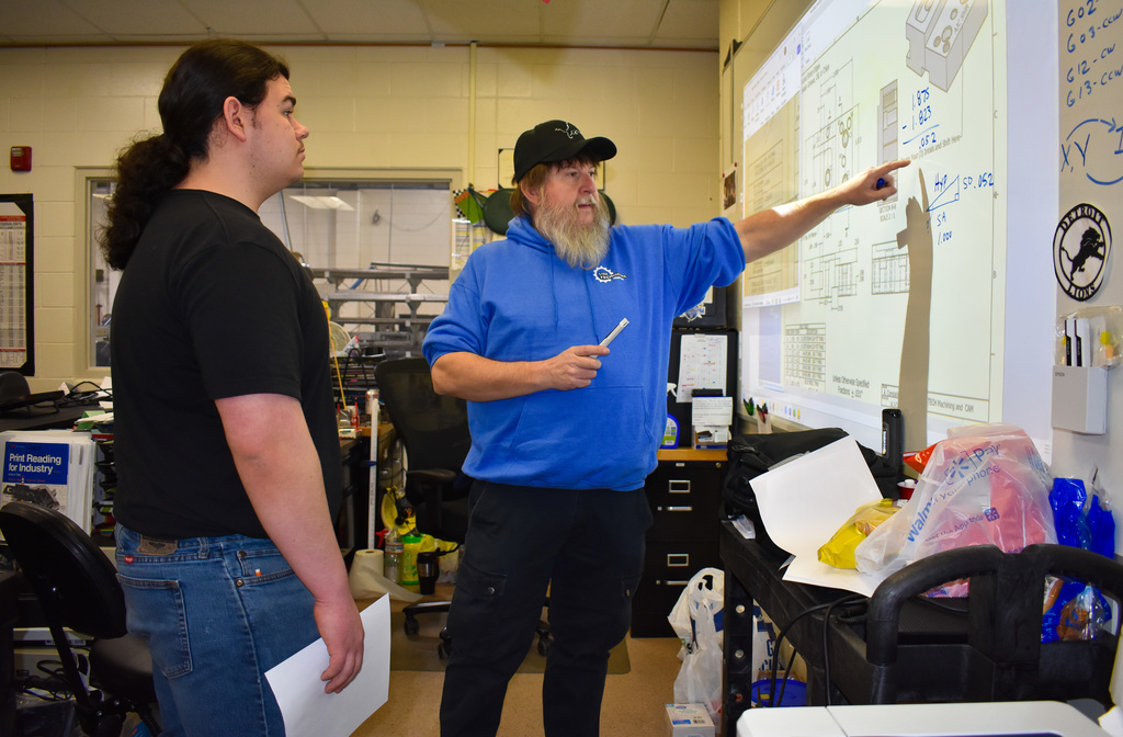 Student and instructor work on a problem using the white board in a classroom
