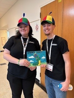 Two students posing with the book they chose for the event and dressed in hats that go with the book