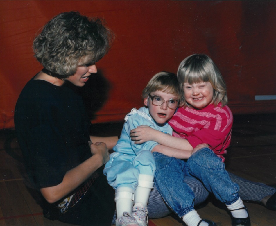 Two students hugging and smiling while an adult looks on 