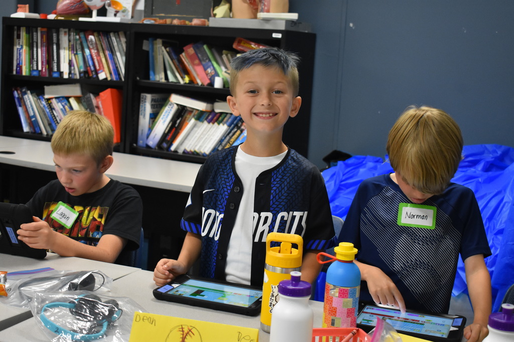 Student smiling for the camera while another works on a tablet