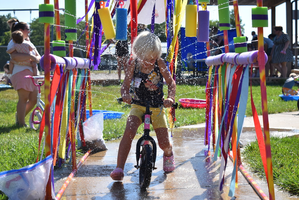Little girl going through the sprinkler on a bike