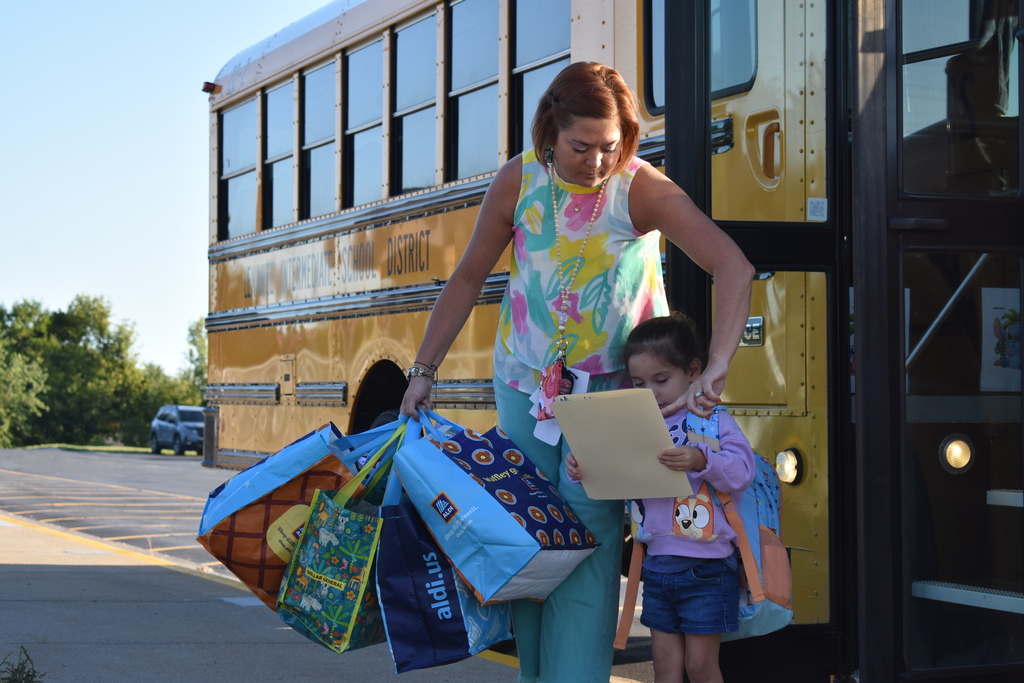 A student exiting the bus as a teacher assists