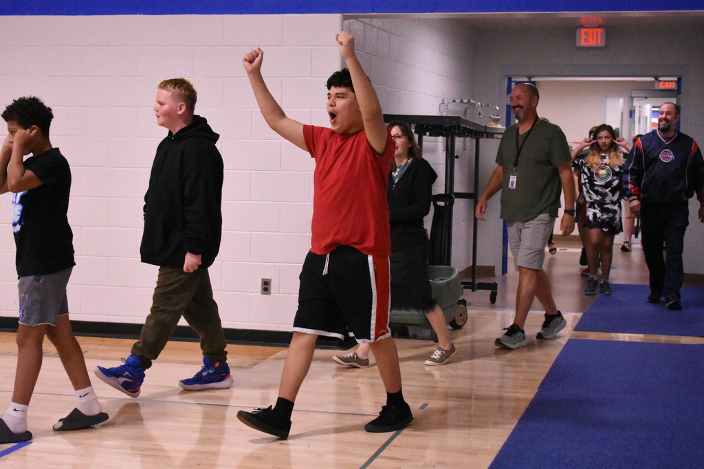 An excited student walking in the gym with other students and staff