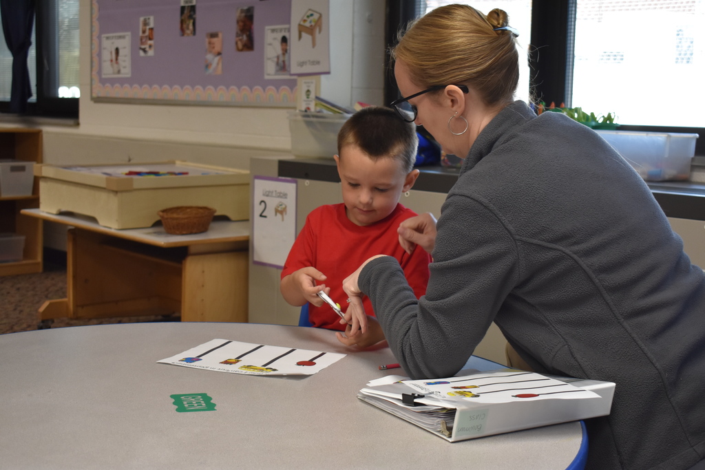 a student learns to use scissors as an instructor assists