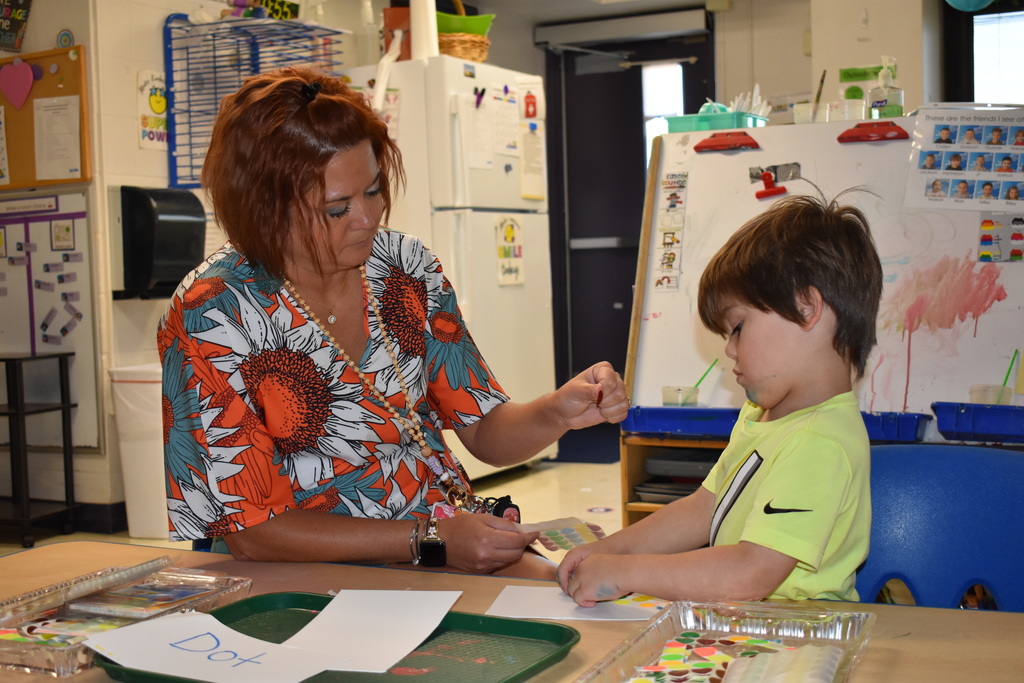 A teacher helps a student with sticker dot art