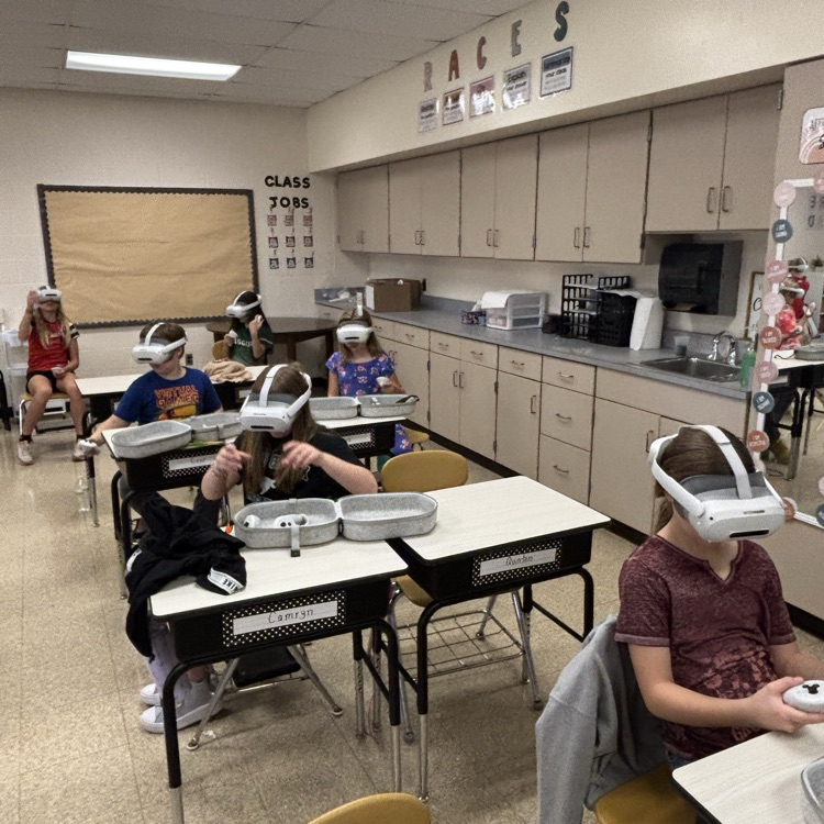 students are seated with headsets on, they hold hand controllers
