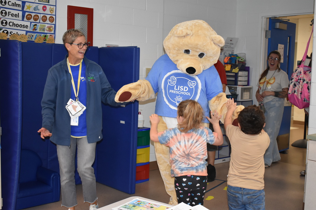 Two students running up to Barry the mascot as a teacher looks on from behind