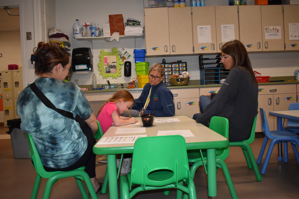Two teachers at a table with a little girl and parent