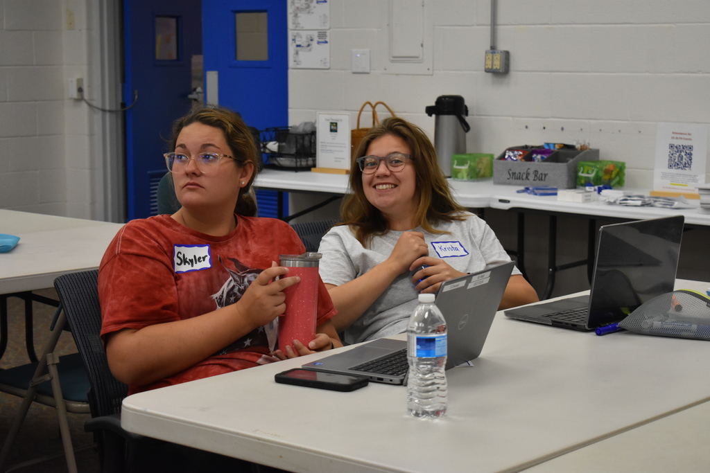 A teacher smiling at the camera with another teacher listening to a presentation