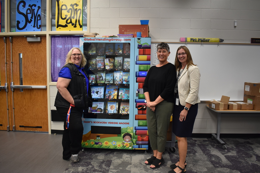 Three educators posing with the book vending machine.