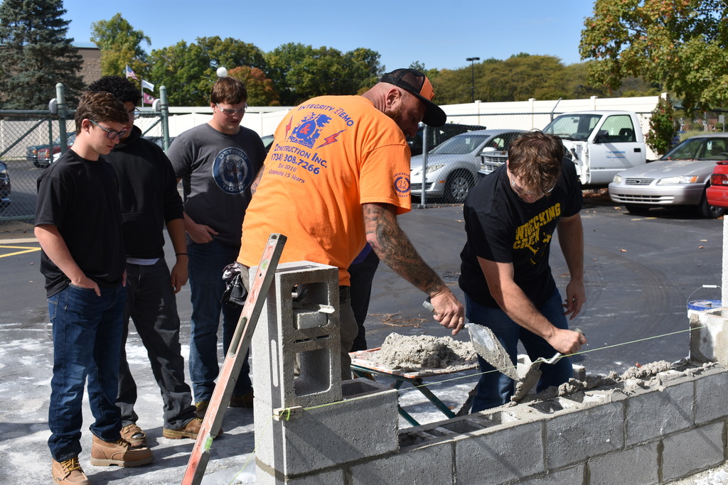 A student practicing laying block with a demonstrator assisting
