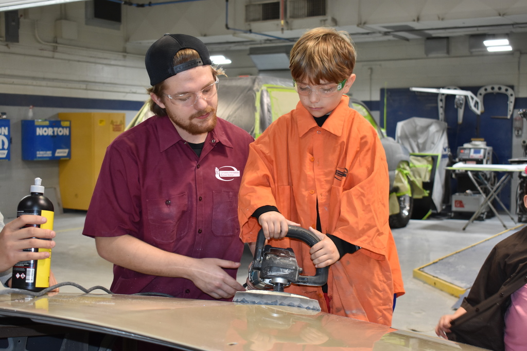 A young student learns how to buff a car with a TECH Student helping