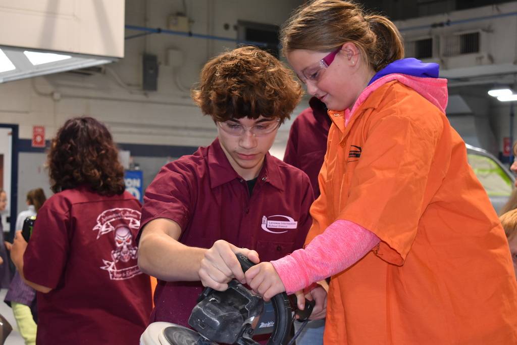 A student learns to buff a car while a TECH student assists