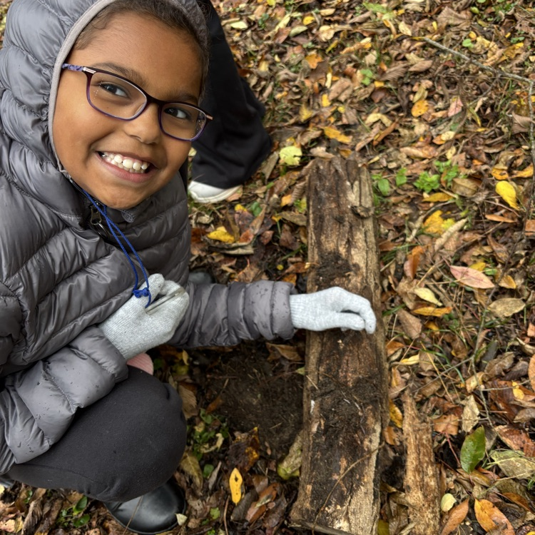 a female student smiles at the camera showing off the earthworm she found on a log