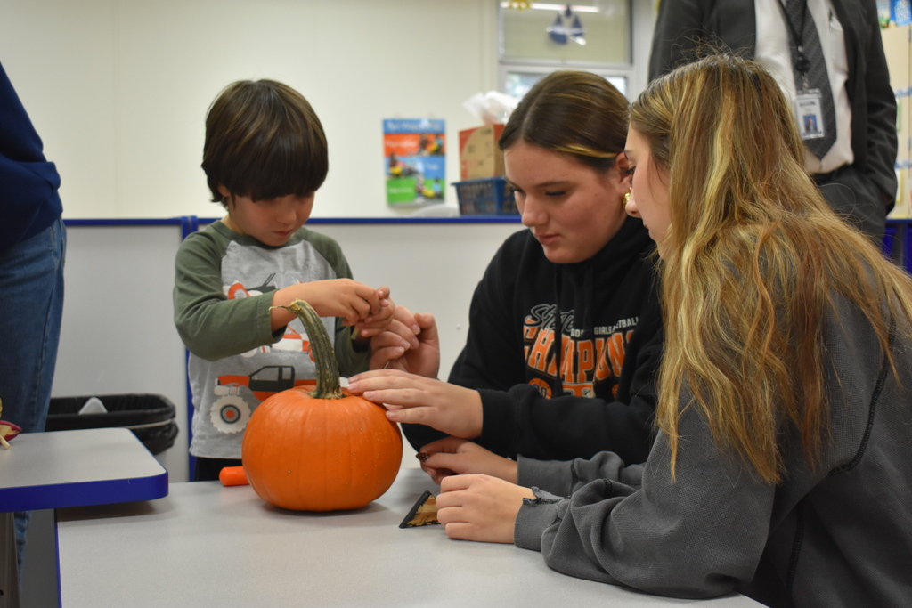 two student volunteers helping a kid with his pumpkin