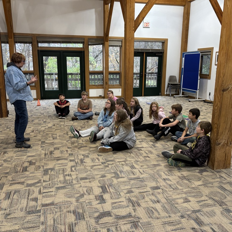 a group of students sit on the ground as they listen to adults 