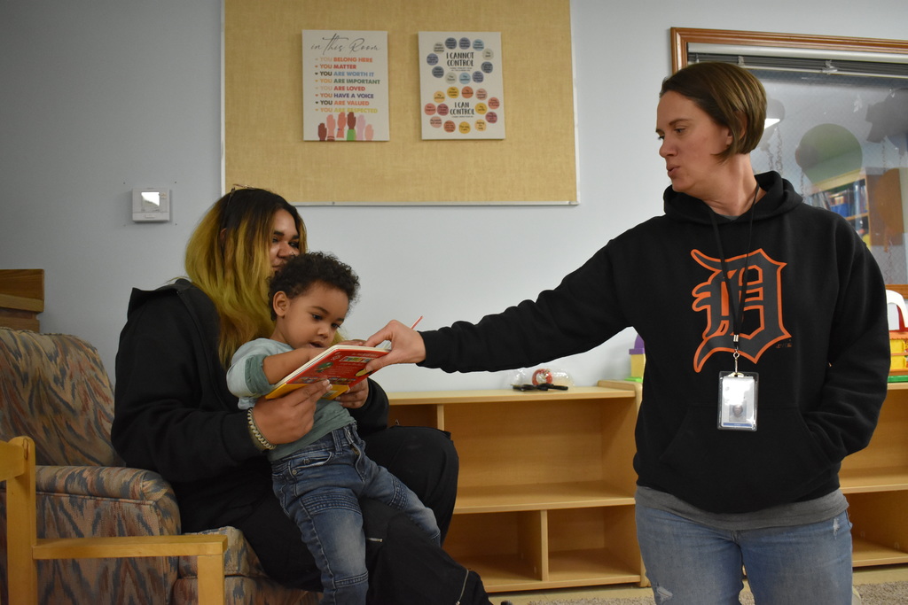 A mom reading with her child while an instructor points at the book with the kid