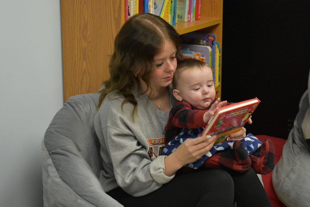 A child in his mom's lap reaching for a book