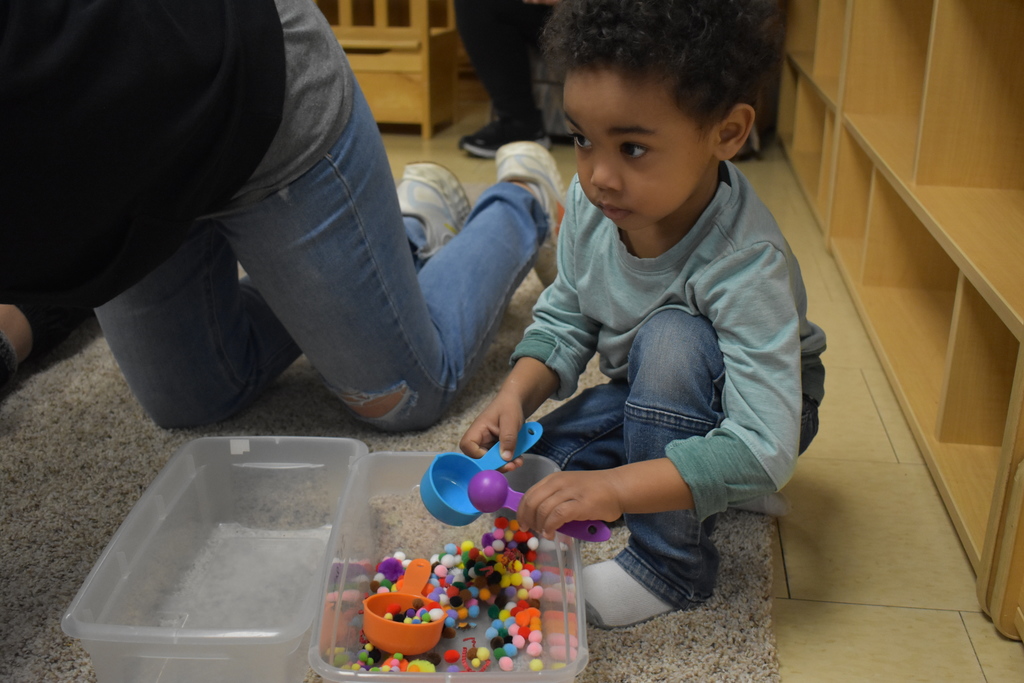 A child playing with poms in a bin