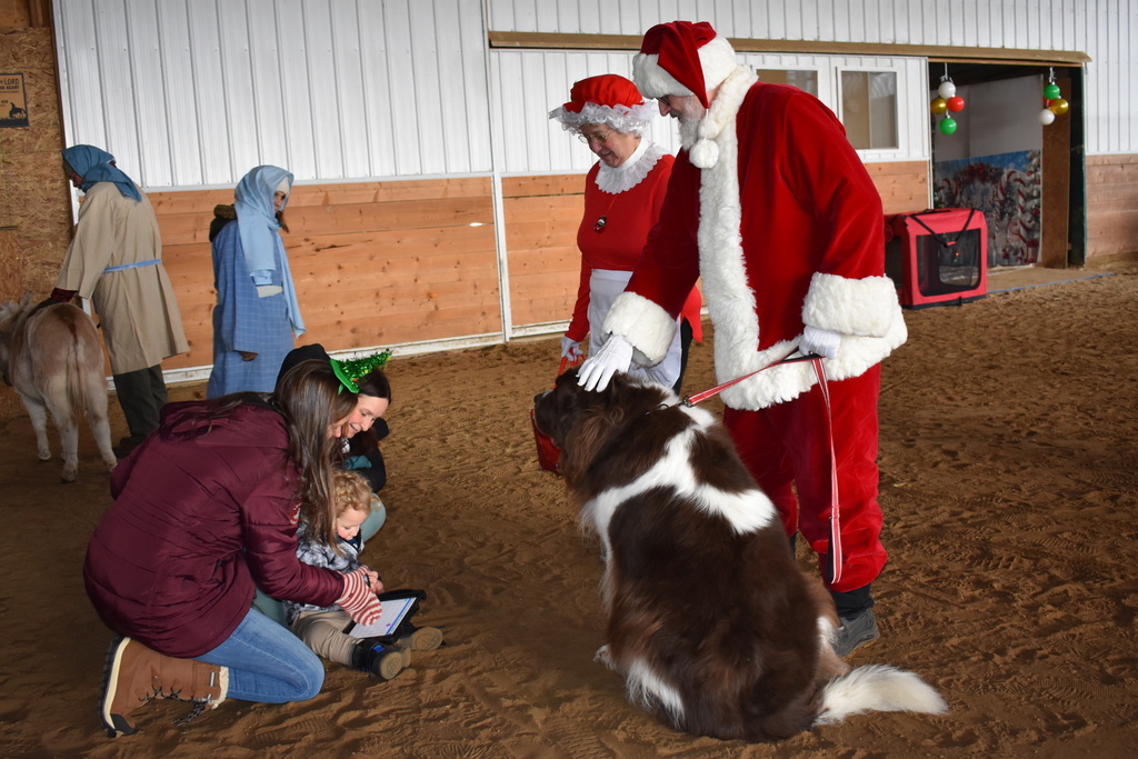 A boy telling santa and mrs. Claus what he wants using a talker with assistant from his mom and teacher