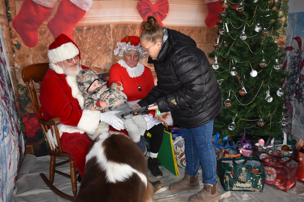 A little boy on Santa's lap while his mom holds his talker to communicate with Santa
