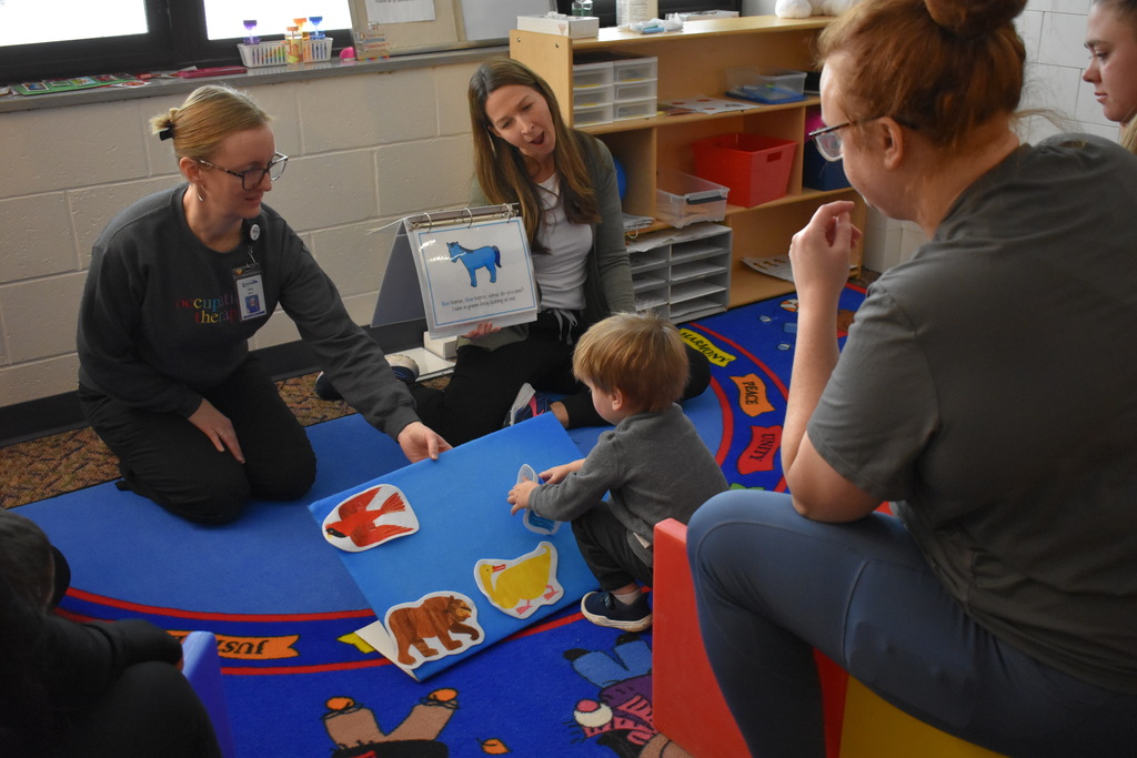 Instructors with a young child as the child places an animal on the felt board