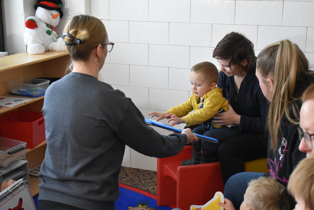 A young child on a parent lap as an instructor hands a felt board to the child