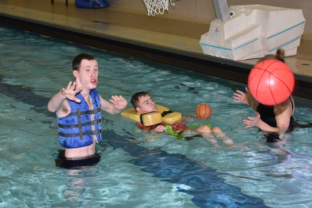 A student threw a ball in the water while another student and instructor swim in the background