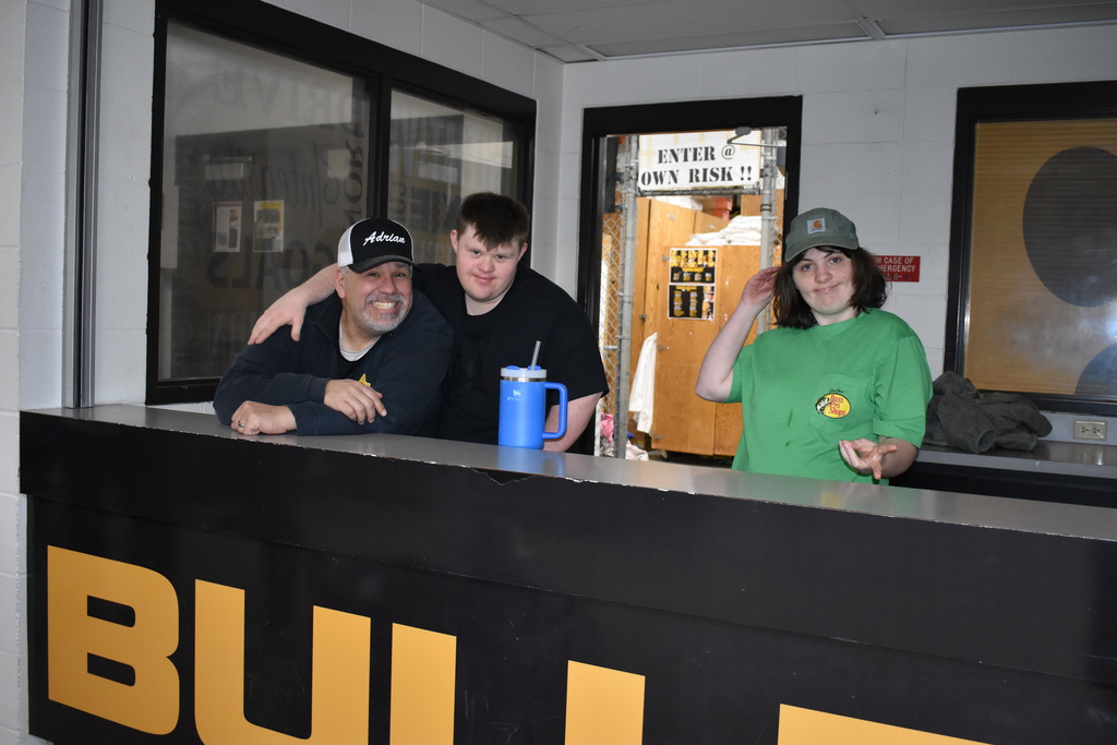 Instructor and two students working behind the desk near laundry at Adrian College