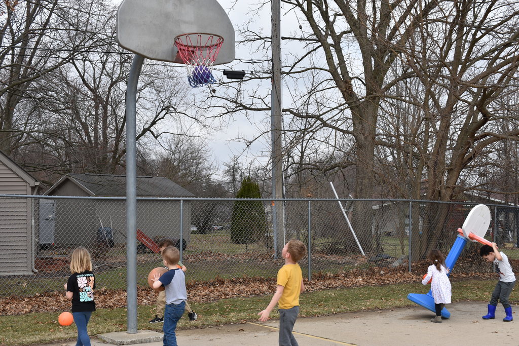 A kid making a basketball shot while other kids play around him