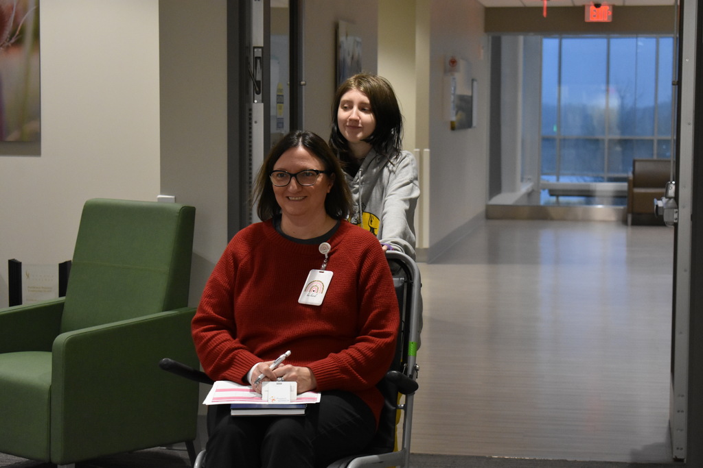 A student demonstrating how to push a patient in a wheelchair with a volunteer in the wheelchair