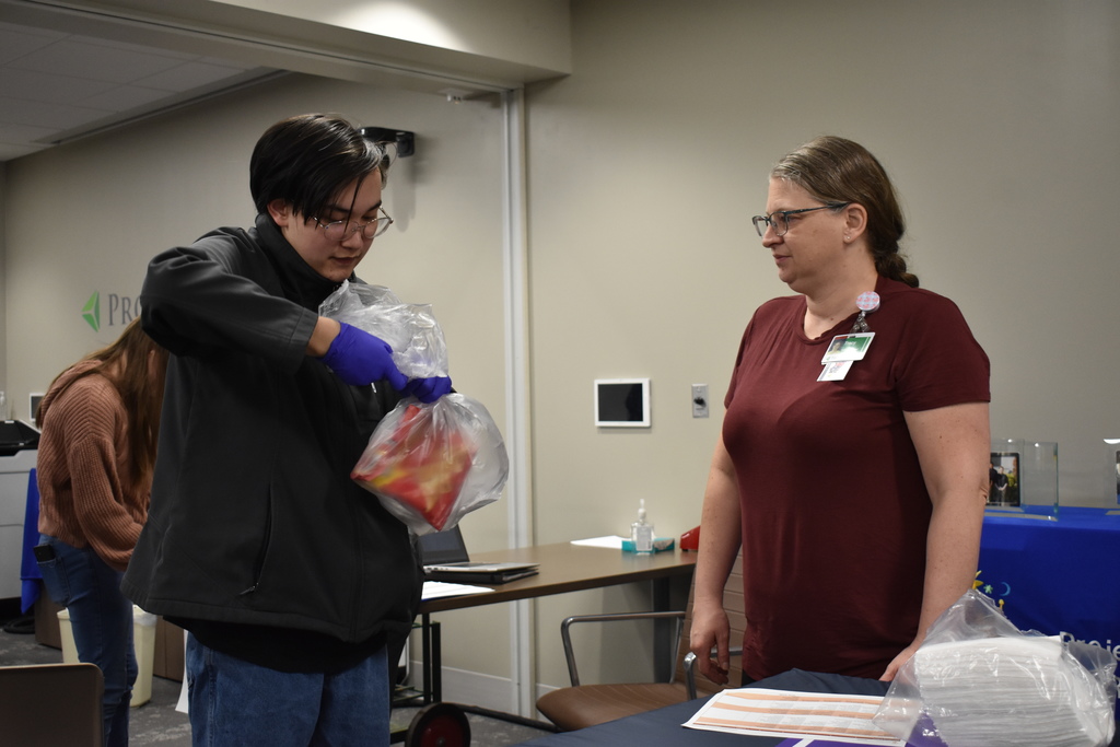 A student practicing how to tie a garbage bag while a volunteer looks on