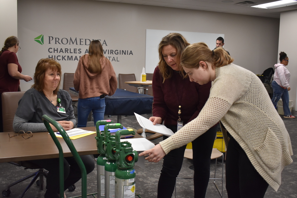 A student following instructions from two volunteers, as she checks levels on tanks
