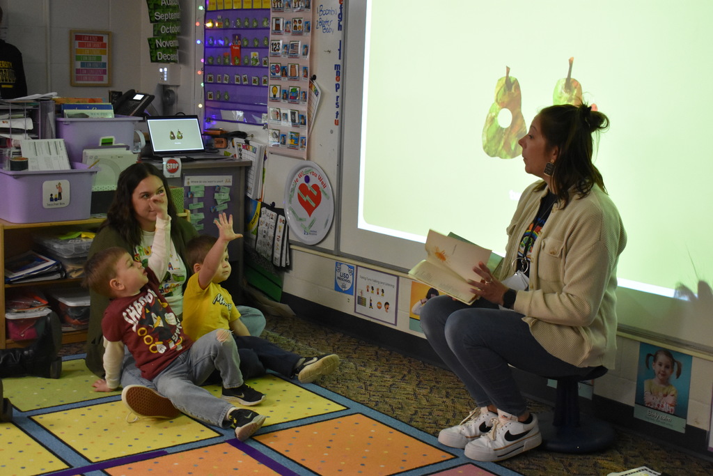 A teacher reading and students raising their hands to questions being asked