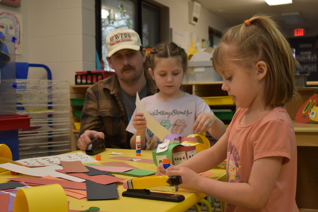 Two students creating art while a parent looks on