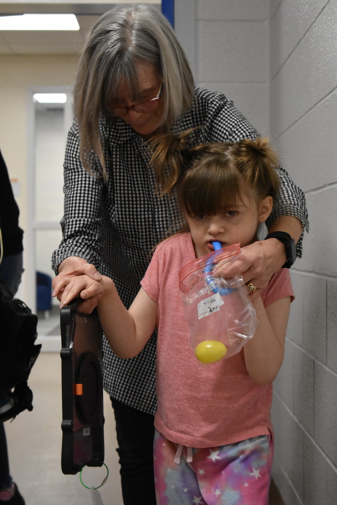 a teacher assisting a student walking as she collects her eggs