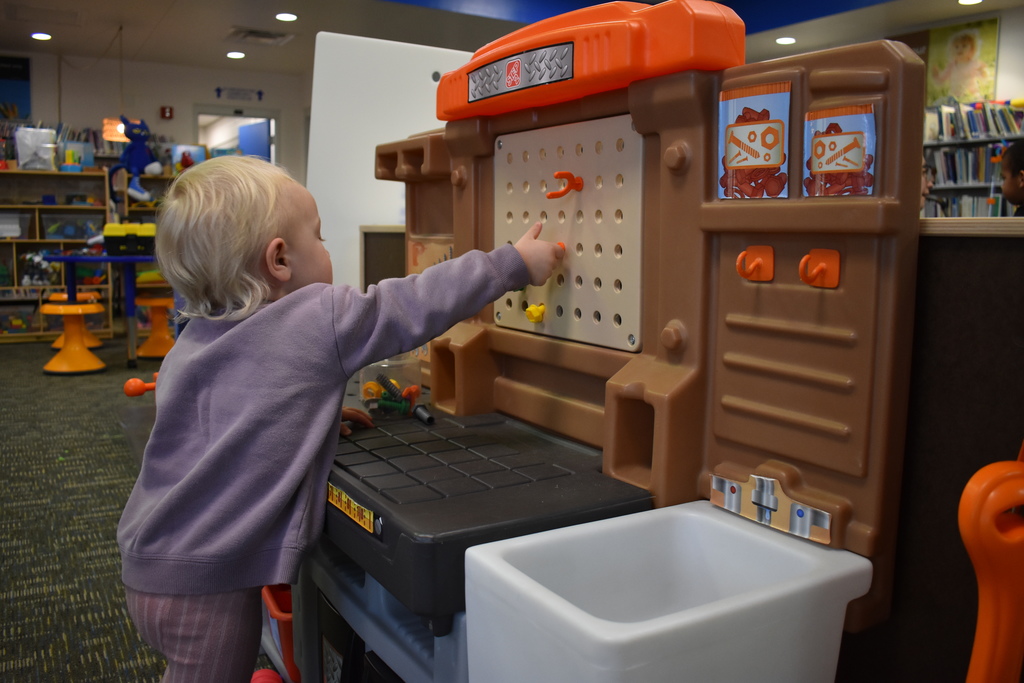 A little girl playing with a tool bench