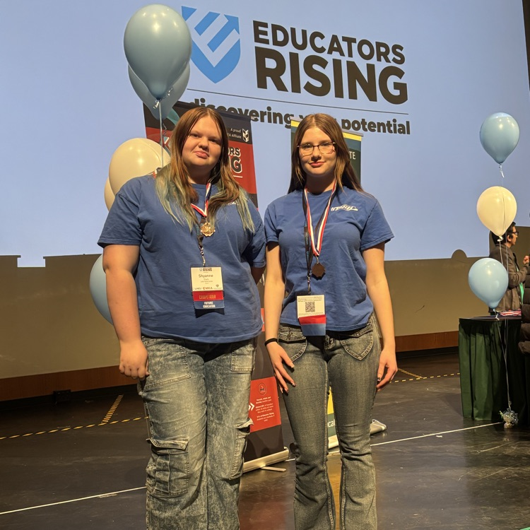 two students posing on stage and smiling 