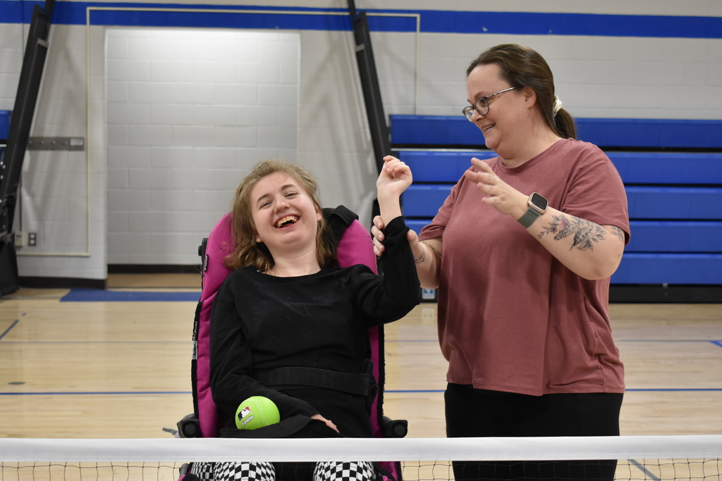A student with a huge smile after releasing the ball with the assistance of a teacher