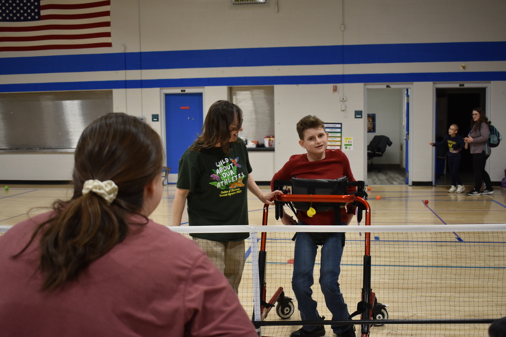 A student preparing to throw a ball toward a teacher with the assistance of a second teacher
